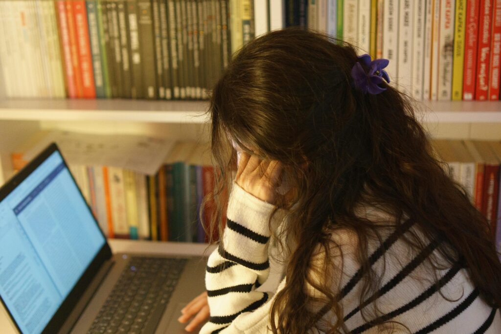 A woman in a library using a laptop, appearing stressed while studying. Perfect for educational or mental health themes.